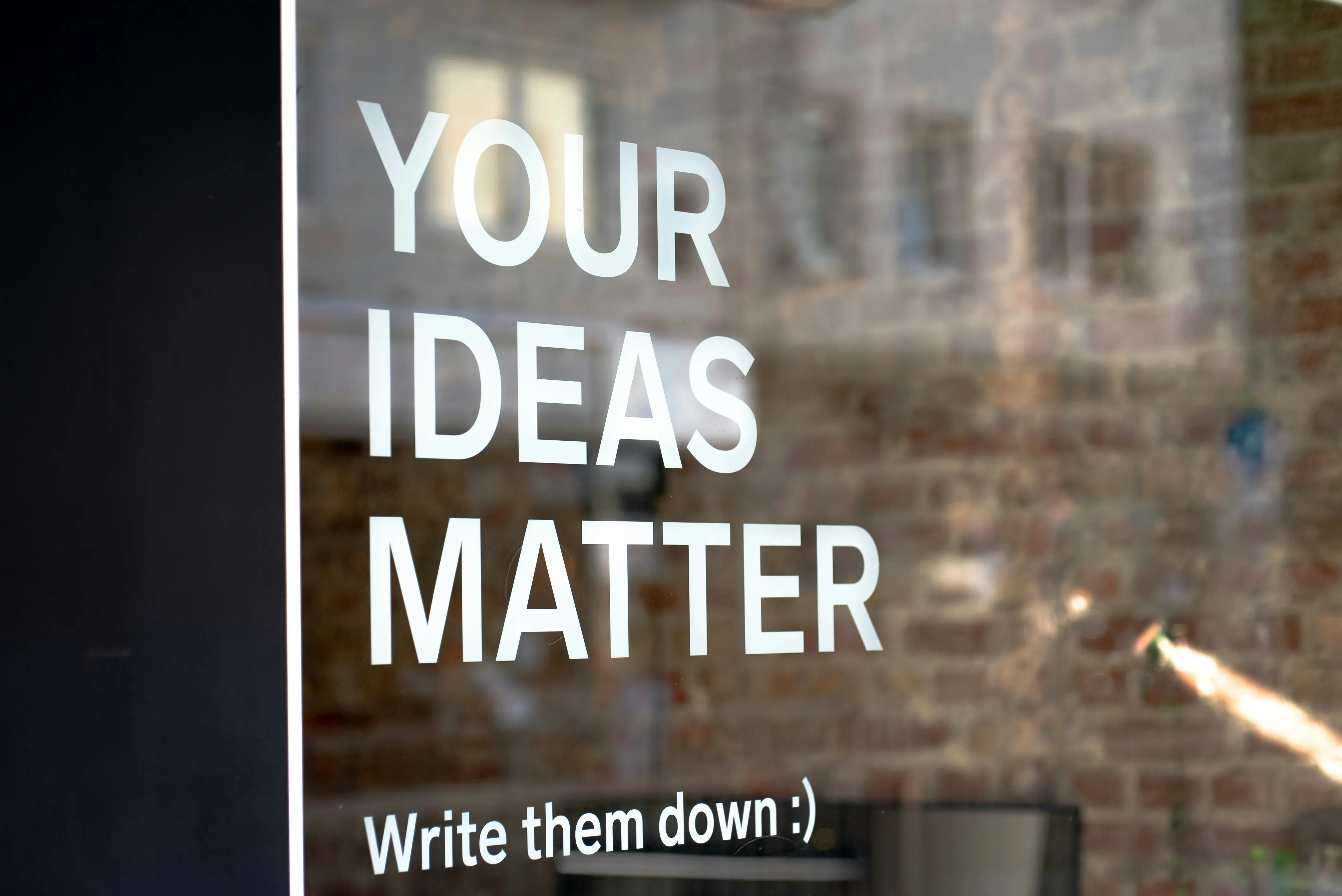 Photograph of a window with white text "Your ideas matter - write them down :)"